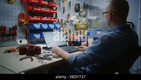 Uomo che controlla le azioni in tempo reale e i grafici del mercato Exchange utilizzando un computer portatile e guarda il tutorial sul trading online su un tablet digitale. Dipendente che studia Trading in remoto durante l'orario di lavoro in officina. Foto Stock