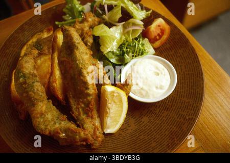 Un piatto di pesce e patatine con spicchi di patate, un contorno di insalata fresca, un spicchio di limone e salsa di tartaro Foto Stock
