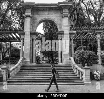 Guanajuato City, Messico - 30 maggio 2016: Una donna cammina oltre i gradini del Jardin de la Union, mentre un uomo siede su una panchina nelle vicinanze. Foto Stock