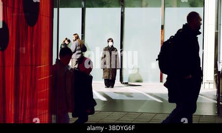 All'esterno dei pianeti TeamLab, un membro del personale mascherato sta alla luce del sole mentre i visitatori passano Foto Stock