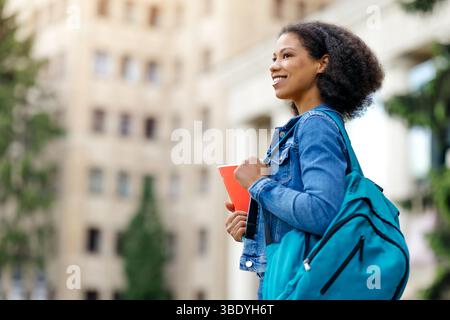 Vista laterale della giovane studentessa afroamericana con zaino e notebook, Foto Stock