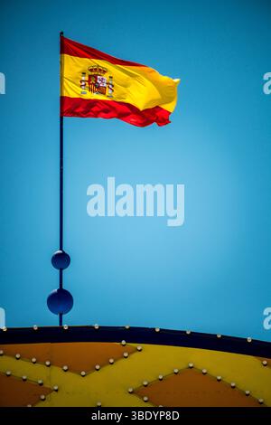 La vibrante bandiera della Spagna ondeggia orgogliosamente sopra il cancello d'ingresso della Fiera di aprile a Siviglia, mostrando l'atmosfera festosa. Foto Stock