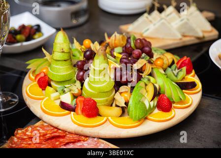Piatto di frutta vivace con pere affettate, uva, arance, fragole, kiwi, e altra frutta fresca, perfetta per feste o catering. Foto Stock