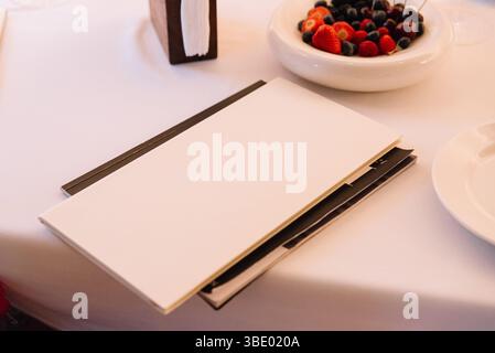 Elegante ambiente da tavola in un ristorante con menu bianco, portasciugamani e una ciotola di frutti di bosco e ciliegie fresche assortite. Foto Stock
