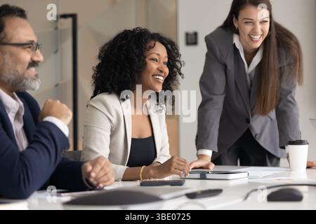 Compagni di squadra multietnici risi che hanno una comunicazione positiva riuniti al tavolo di conferenza Foto Stock