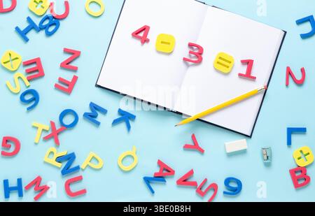Equazione matematica con numeri e simboli sul notebook con lettere alfabetiche colorate sparse su sfondo azzurro. Ritorno al concetto di scuola. Foto Stock