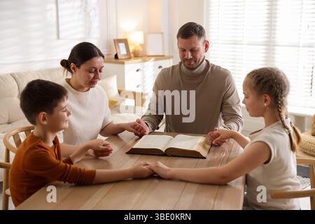 Famiglia con la Bibbia che prega a tavola all'interno Foto Stock