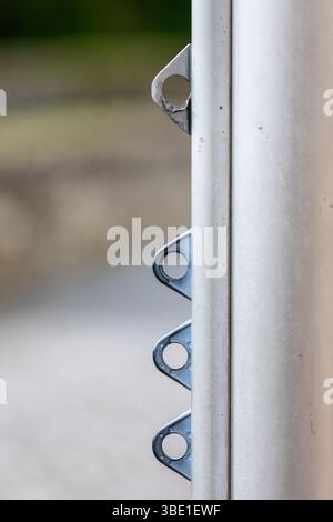 Primo piano di un palo metallico con diversi occhielli triangari, probabilmente utilizzati per fissare corde di bandiere o cavi, contro una b leggermente sfocato Foto Stock