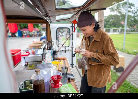 Barista maschile indonesiano del sud-est asiatico che serve un caffè. Una piccola azienda di un bar o di un bar su un camion Foto Stock