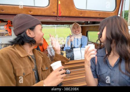 Coppia indonesiana del sud-est asiatico che si gusta un caffè di fronte alla caffetteria. Una piccola azienda di un bar o di un bar su un camion Foto Stock