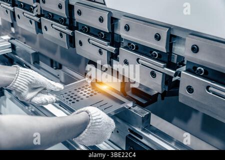 L'operatore tecnico che lavora con la lamiera sul freno della pressa idraulica CNC. Mette la parte e la piega in una grande macchina ad angolo. Foto Stock