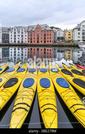Kayak gialli luminosi ormeggiati sulle acque calme del canale di Brosundet ad Alesund, Norvegia, con colorati edifici in stile Art Nouveau riflessi sullo sfondo Foto Stock