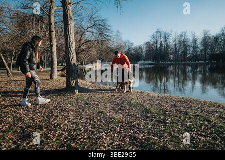 Una coppia gode di una passeggiata al tramonto nel parco con il proprio cane vicino al tranquillo lago. Foto Stock