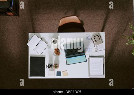 Area di lavoro organizzata che mostra laptop, blocchi appunti, tazze da caffè e impianti. Vista dall'alto che rivela varie forniture per ufficio disposte sulla scrivania Foto Stock