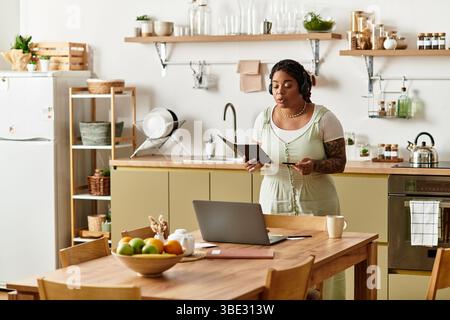 Una giovane donna afroamericana si impegna con il suo laptop mentre lavora dalla sua accogliente cucina. Foto Stock