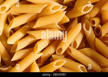 Primo piano di penne crude. Colore giallo oro. Ingrediente italiano per alimenti secchi. Cucina mediterranea tradizionale. Prodotto ricco di carboidrati. Foto Stock