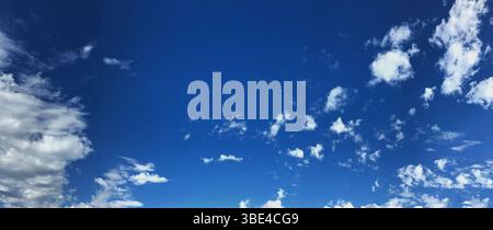 Un'ampia vista panoramica di un cielo blu vibrante con soffici nuvole bianche sparse. Il tranquillo paesaggio funge da sfondo rilassante adatto alla digitazione Foto Stock