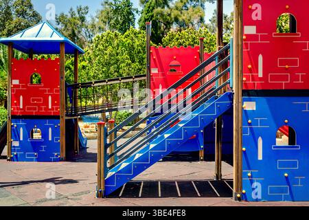 Parco giochi per bambini luminoso e colorato con strutture a tema castello, scivoli, scale e ponte di corda. Area giochi all'aperto nel parco, giorno di sole Foto Stock