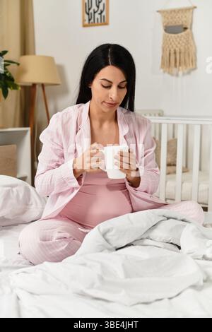 La giovane donna ama una tazza nel suo spazio accogliente, abbracciando la gravidanza. Foto Stock