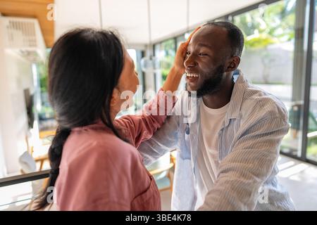 Giovani coppie diverse che sorridono gioiosamente insieme nel loro luminoso soggiorno, indossando abiti casual Foto Stock