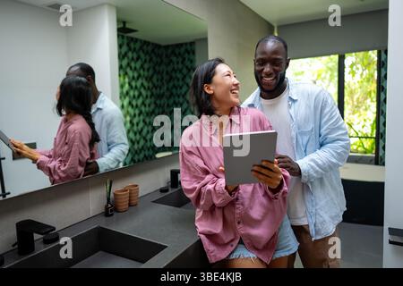 Felice coppia multietnica che utilizza un notebook, acquista online con le vendite, gioca insieme Foto Stock