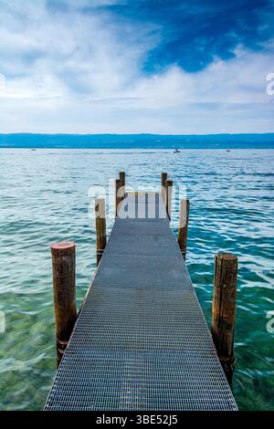Un robusto molo si estende nelle tranquille acque del lago Leman, circondato da affascinanti sfumature blu e da un'atmosfera tranquilla. Alta Savoia. Francia Foto Stock