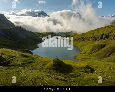 Una vista mozzafiato del tranquillo Bachalpsee in Svizzera, circondato da lussureggianti colline verdi e lontane montagne alpine, sotto un cielo ricoperto di c Foto Stock