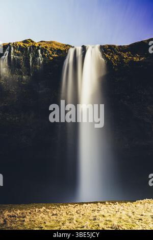 Una vista mozzafiato di una maestosa cascata Seljalandsfoss che si getta su un'aspra scogliera in Islanda. La luce del sole illumina l'acqua nebbiosa, la creatina Foto Stock