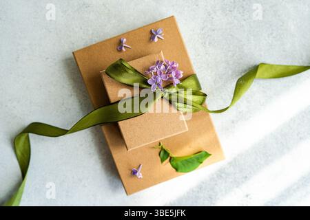 Due scatole regalo marroni adornate con nastro verde e fiori viola, per una presentazione elegante. Un concetto perfetto per festeggiamenti o occasioni speciali Foto Stock