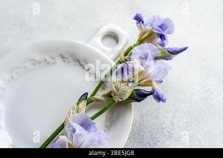 Dall'alto eleganti fiori viola Iris che si trovano su un piatto di ceramica vintage, adagiato su uno sfondo grigio testurizzato, creano un'atmosfera rinfrescante e piacevole Foto Stock