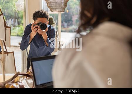 Un fotografo in un negozio di borse utilizza una fotocamera per catturare i momenti più belli. La luce naturale del punto vendita e gli eleganti espositori a sacco creano uno sfondo meraviglioso per la creatura Foto Stock