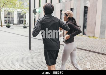 Una coppia che fa jogging insieme in un ambiente urbano, che mette in mostra uno stile di vita attivo. Si vedono da dietro, si godono l'aria fresca e si mantengono in forma Foto Stock