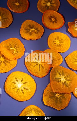 Fette di cachi secchi, luminose e traslucide, disposte artisticamente su un vivace sfondo viola, che mostrano i loro motivi unici simili a stelle. Foto Stock