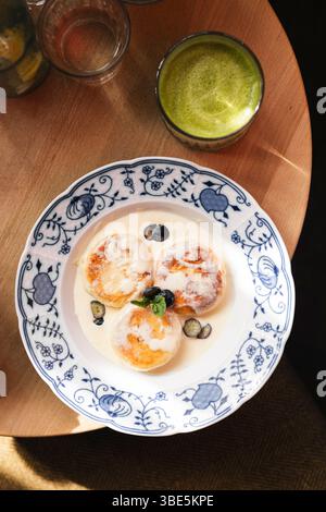 Vista dall'alto di una sana colazione con frittelle di formaggio ricoperte di bacche e sciroppo d'acero su un piatto decorativo blu e bianco, con Foto Stock