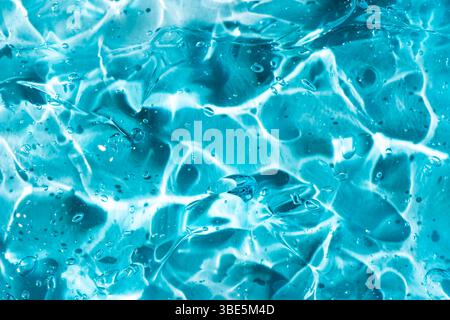 Primo piano di un gel blu che mostra i modelli e le trame astratte dei fluidi. La superficie liscia riflette la luce, creando un'interazione dinamica delle luci Foto Stock