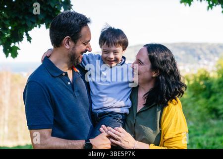 Una famiglia gioiosa condivide un momento d'amore in un ambiente panoramico all'aperto, mettendo in risalto l'Unione e la felicità. I genitori tengono il loro figlio sorridente con D. Foto Stock
