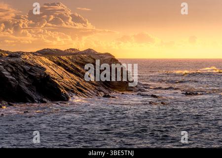 Spettacolare costa rocciosa con formazioni geologiche a strati al tramonto dell'ora d'oro. Onde che si infrangono contro scogliere stratificate, calda luce serale, rugge Foto Stock