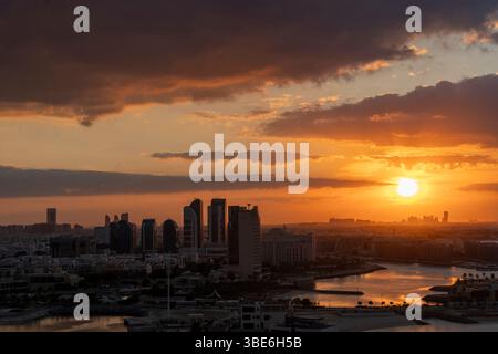 Il tramonto mette in risalto lo skyline di Abu Dhabi con grattacieli sagomati e acqua che riflettono il cielo dorato degli Emirati Arabi Uniti. Foto Stock