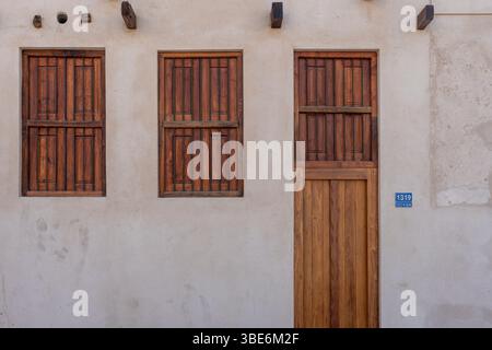 Due finestre in legno e una porta creano una facciata simmetrica alla al-Jalahma House sul Pearling Path a Muharraq sotto la luce del sole. Foto Stock