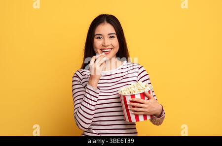 Una giovane donna sorridente ama i popcorn con uno sfondo giallo brillante Foto Stock