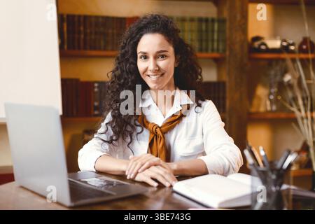 Donna sicura in posa seduta alla scrivania con il computer portatile Foto Stock