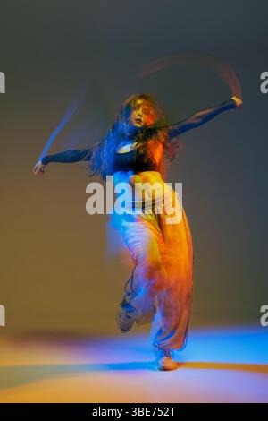 Ballerina jazz-funk in movimento con scintillanti percorsi al neon e illuminazione vibrante, catturata in un'energica esibizione in studio. Foto Stock