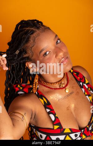 Primo piano verticale di una bella giovane donna con i capelli intrecciati che indossa abiti tradizionali e posa per la fotocamera. Isolato su color senape Foto Stock