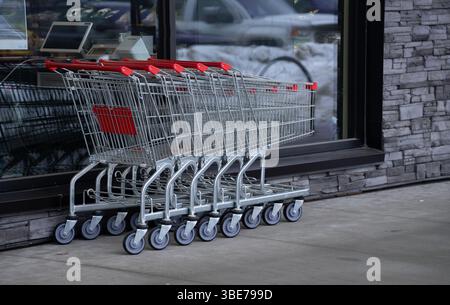 cinque carrelli vuoti montati all'esterno del negozio di alimentari, in acciaio inossidabile o metallo, con ruote e maniglie rosse sovrapposte all'esterno di groce Foto Stock