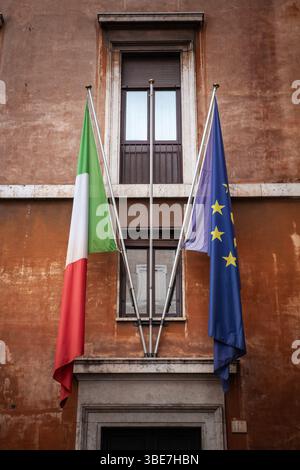 La bandiera italiana e la bandiera dell'Unione europea sono appese in una disposizione a forma di V fuori da un edificio in terracotta di Roma, l'Italia è uno dei membri fondatori dell'UE e un lea Foto Stock