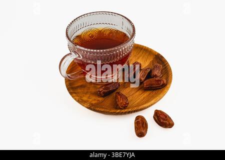 Accanto a un piatto di legno pieno di datteri freschi si trova un bicchiere di tè splendidamente lavorato. I colori caldi creano un ambiente invitante e tradizionale. Foto Stock
