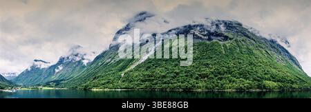 Ampio angolo panoramico del lussureggiante paesaggio di fiordi nella Norvegia occidentale, con montagne avvolte dalle nuvole e acque riflettenti. Foto Stock