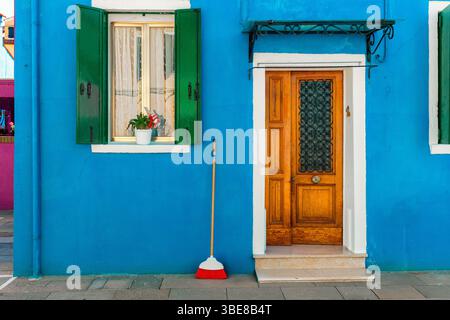Una casa blu brillante con persiane verdi vibranti e porta in legno arancione a Burano, Italia. Foto Stock
