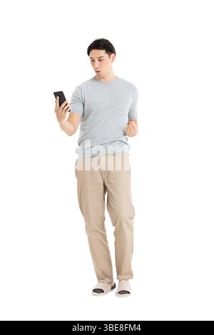 Un giovane che fissa il suo schermo del telefono, assolutamente entusiasta con il braccio alzato in alto Foto Stock