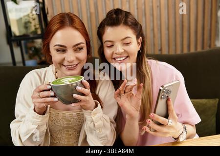 Due bellissimi amici si godono un drink mentre catturano momenti di gioia sul loro telefono. Foto Stock